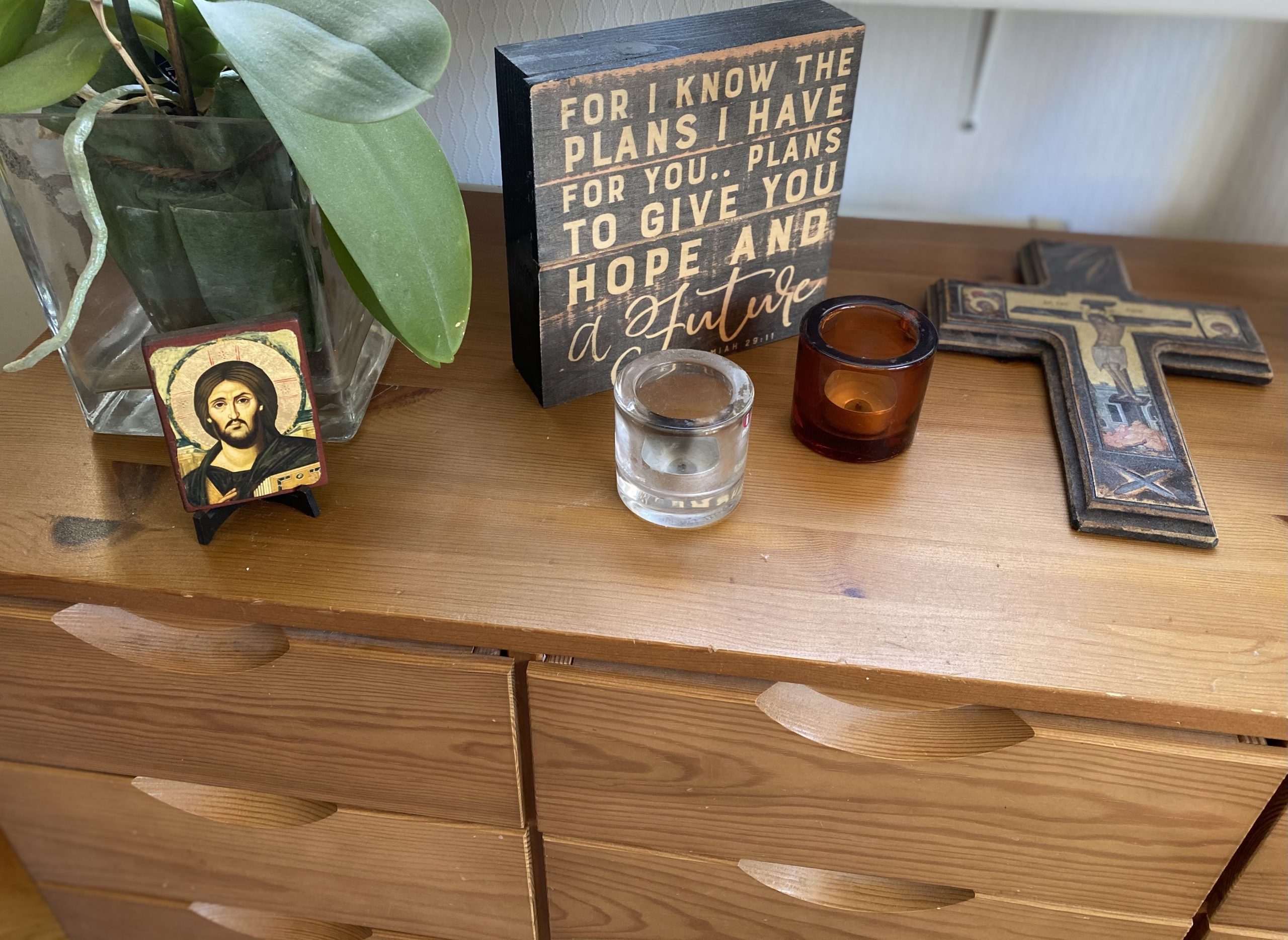 Kotialttari lipaston päällä; kukkamaljakko, pieni Kristusikoni, kaksi tuikkukynttilää, ristinmuotoinen krusifiksi ja huoneentaulu.